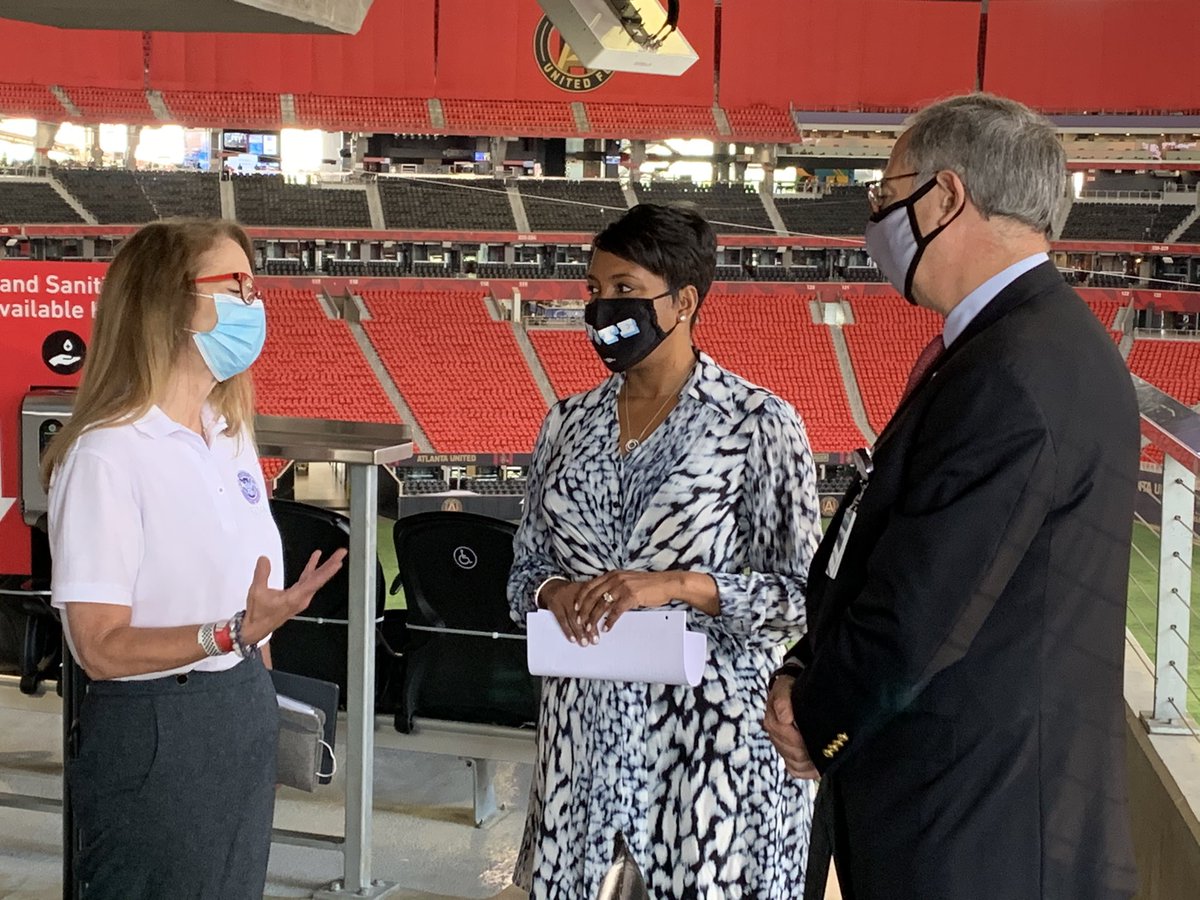 Three people stand in group. Stadium seats behind them.