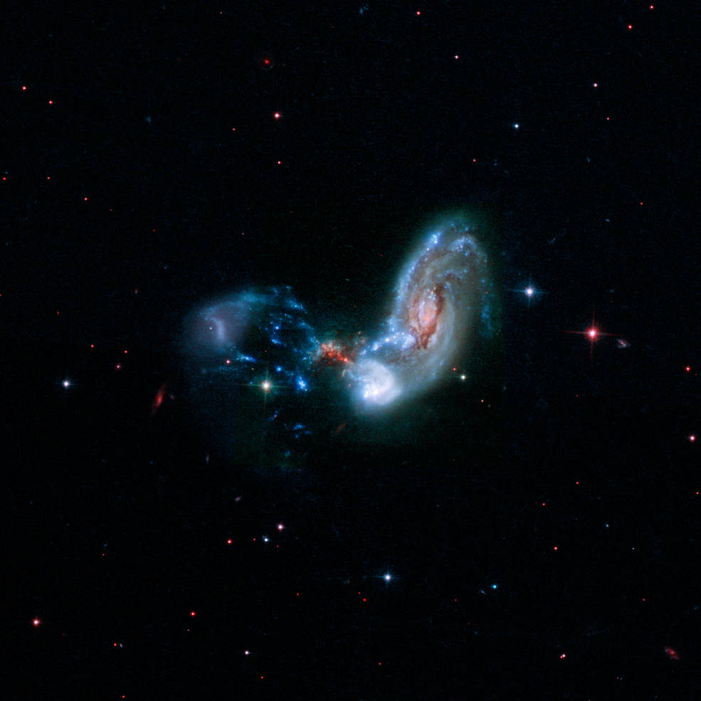 These merging galaxies, known as II Zw 096, are the site of a spectacular burst of star formation that is hinted at in the red speckles near the middle of the image. The image above combines near-infrared, visible, and far-ultraviolet observations from the Hubble Space Telescope.