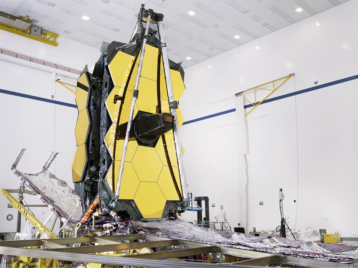 Partially stowed James Webb Space Telescope in the Northrop Grumman cleanroom, taken during integration of its two halves in August 2019. Its giant hexagonal mirrors are folded back on either side, and its 5-layer sunshield is de-tensioned and packed.