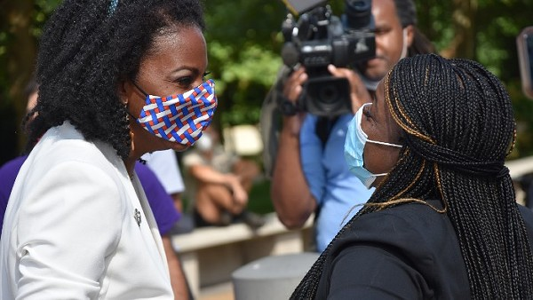 Cori Bush and Tishaura Jones, wearing masks, looking at each other with happy expressions.