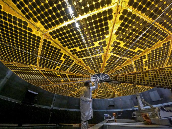 Technician stands beneath a 24-foot-wide, gold-hued spacecraft solar panel