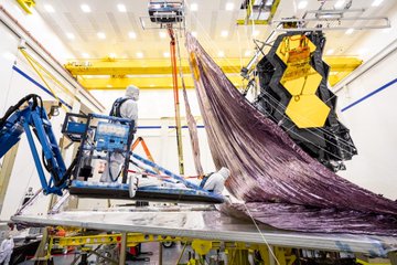 Technicians work together to lift up the James Webb Space Telescope's flattened sunshield in preparation for the folding process.