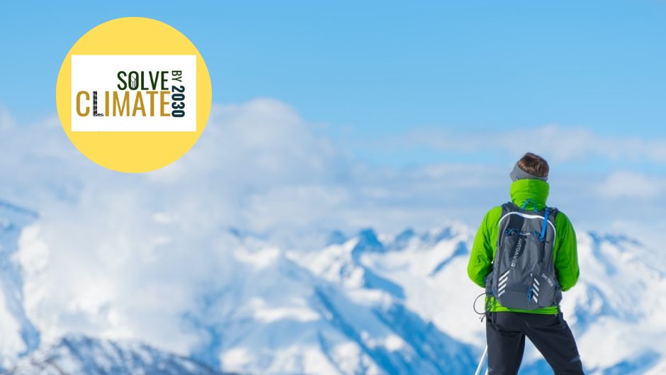 A photo overlooking snowy mountains and a blue sky with a skier in a green coat and the Solve Climate by 2030 logo in the top left corner.