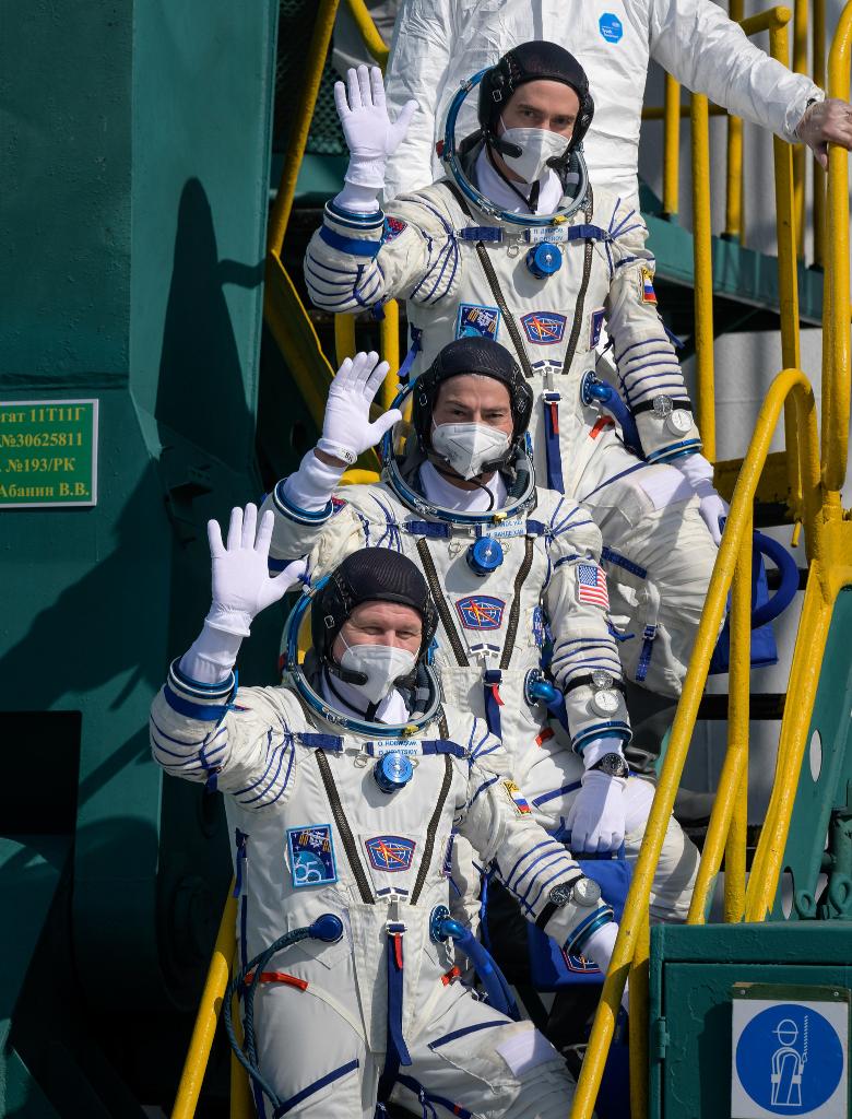 NASA astronaut and two cosmonauts in Sokol suits wave before boarding Soyuz