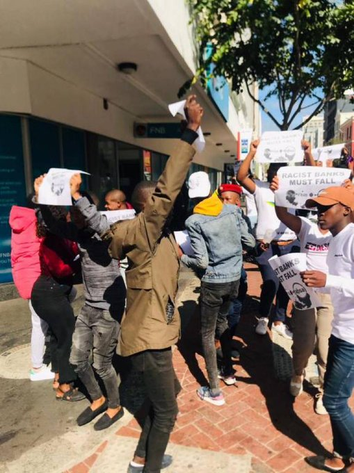 On Friday there was a "spontaneous" protest outside (and inside) a FNB branch in Cape Town. It was publicised by some pictures included in tweets with the hashtag "RacistBanksMustFall".What was it all about? A thread...