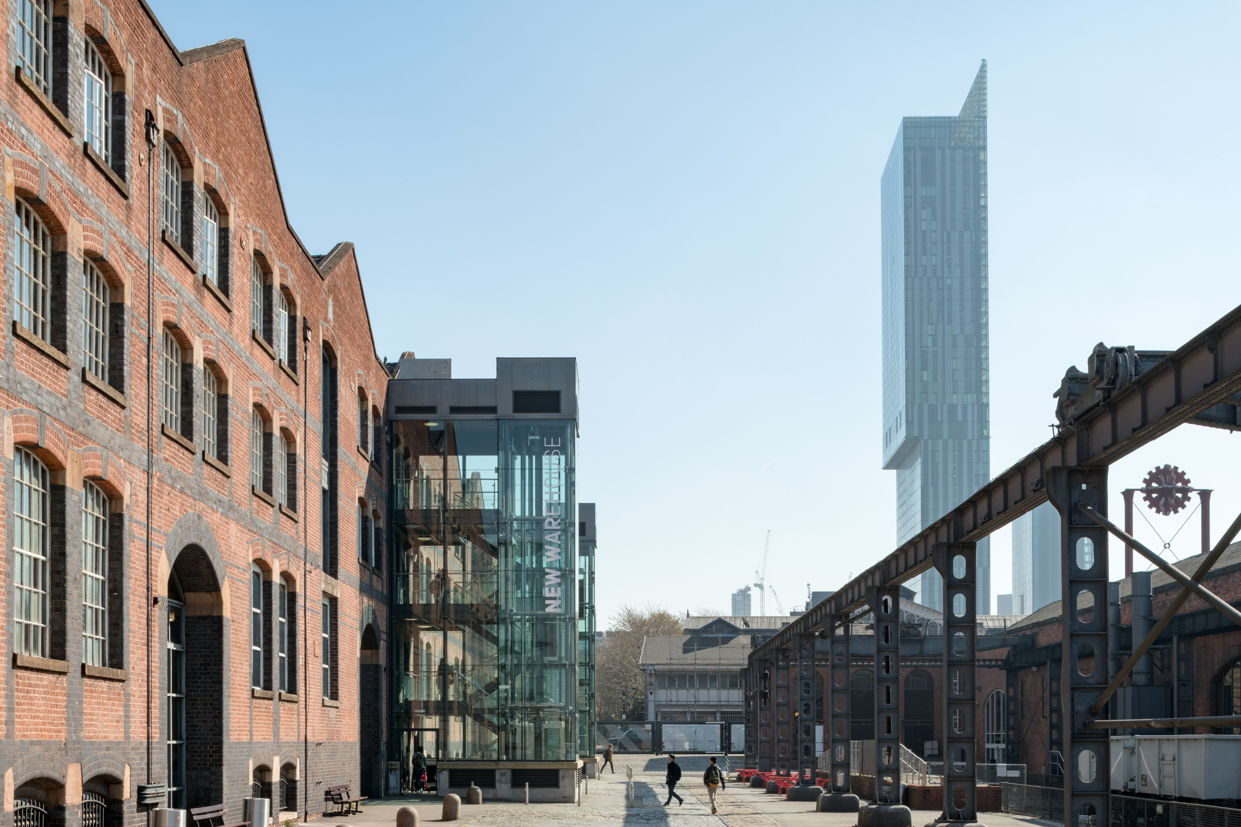 A view of the Upper Yard of the Science and Industry Museum. The large red brick building on the left is the New Warehouse, an industrial era warehouse with large paned windows and modern glass stairwells. The Beetham Tower glass skyscraper can be seen beyond the site to the right.