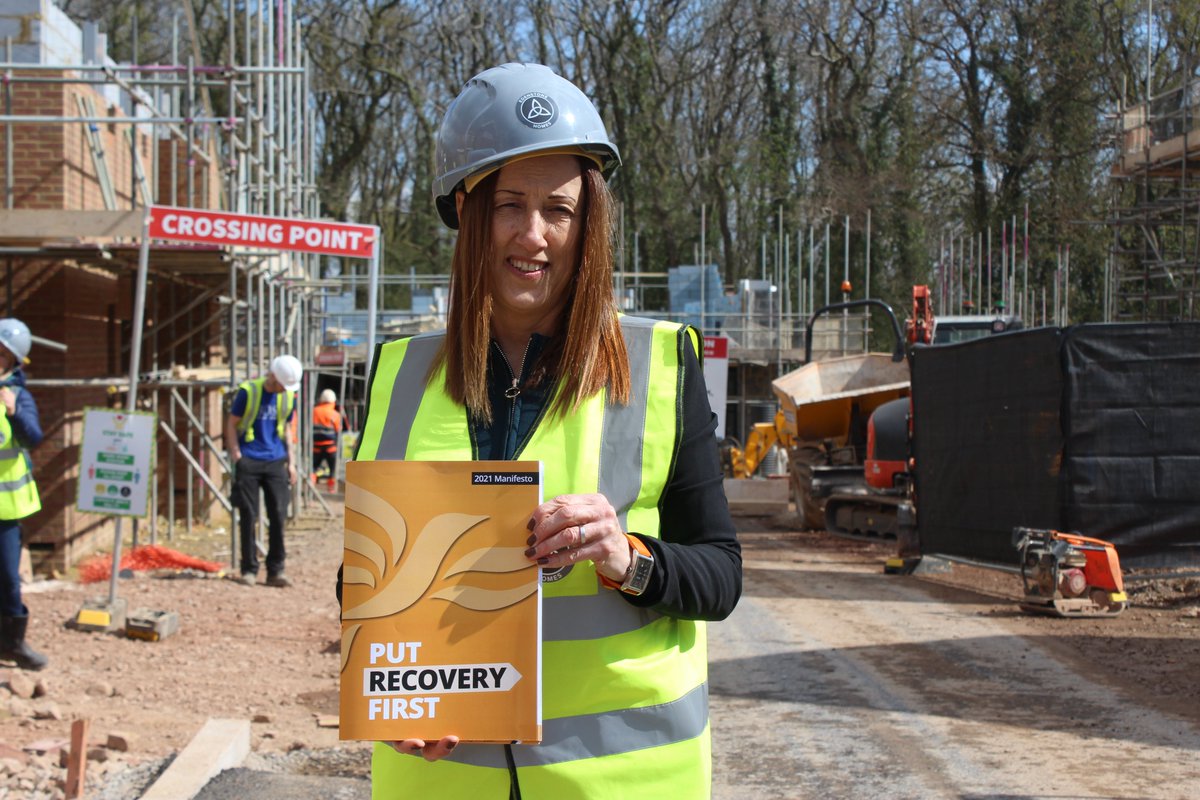 Jane Dodds in a hard hat and high-visability jacket standing in front of a building site. She is holding a copy of our manifesto - entitled 'Put Recovery First'.