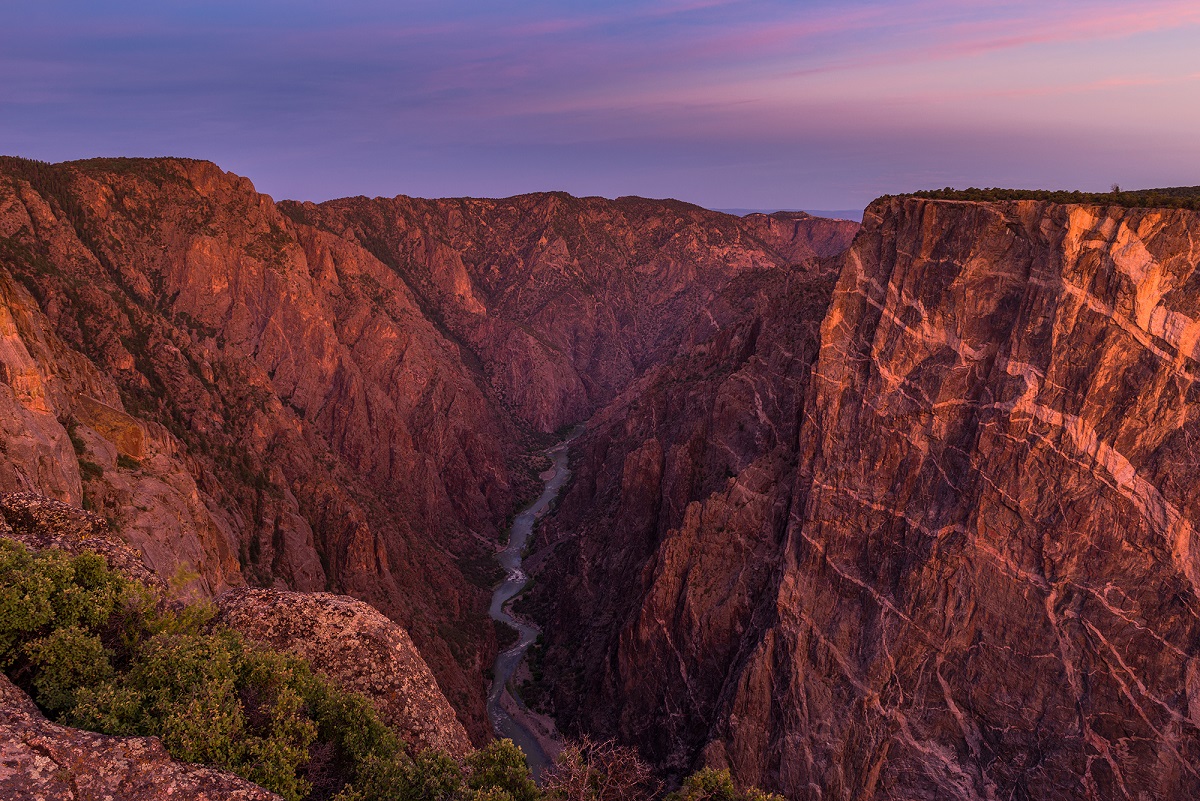 The high walls of the canyon reflect the sunlight as they surround a winding river