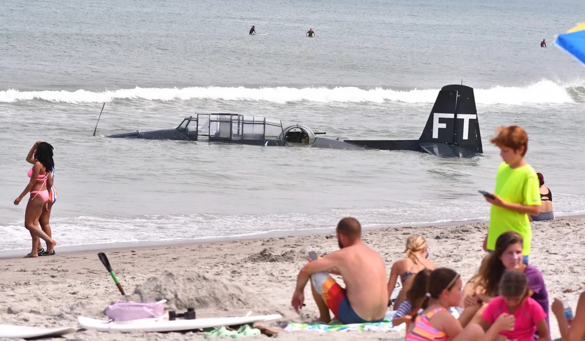 Families and friends on the beach chat as the World War II-era plane is submerged in the background.
