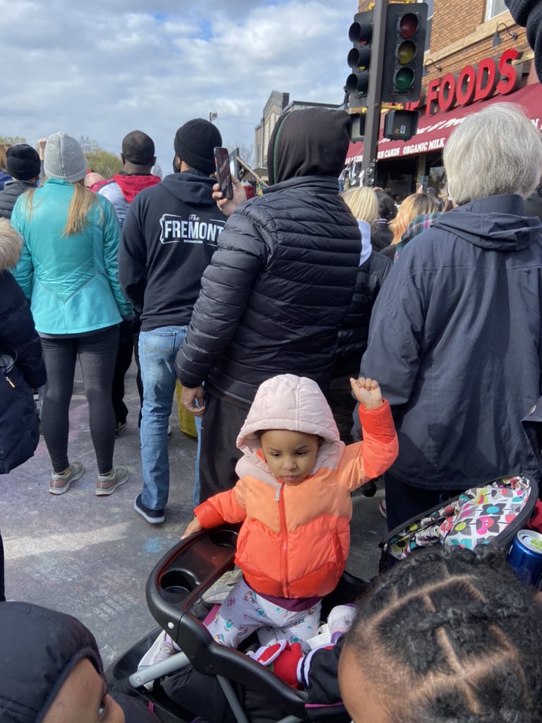 People (of all ages) raise their hands in honor of George Floyd. There are hundreds here, gathered at the spot where he died and posted up on a billboard that reads “All mothers were summoned when George Floyd called for his momma”