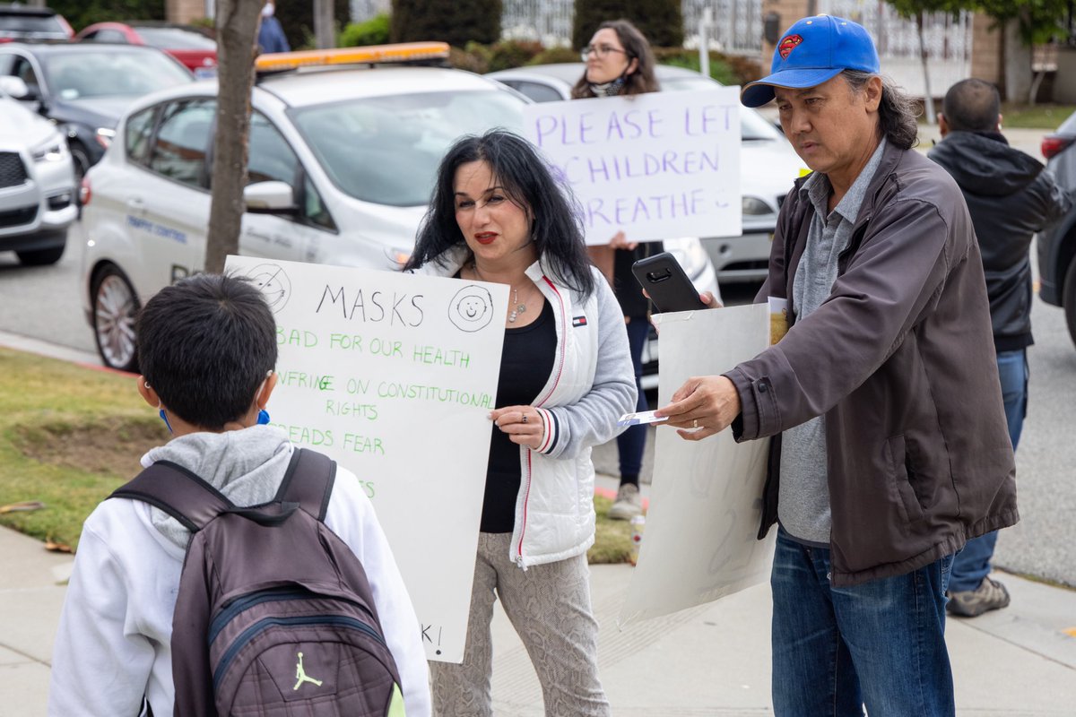 A photo from the event. An anti-mask protester tries to hand out what appears to be a business card to an elementary student.