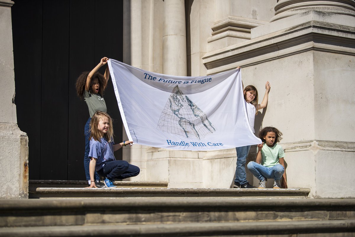 A flag held by four young girls that reads The Future is Fragile, Handle with Care