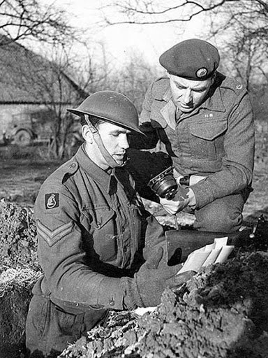 Cpl Robert Bruce Pass from Brixton, London of the 1/5th Bn Queen's Royal Regt, photographed with BBC War Correspondent Frank Gillard recording in a slit trench just behind the front lines a broadcast to go out on Christmas Day 1944.