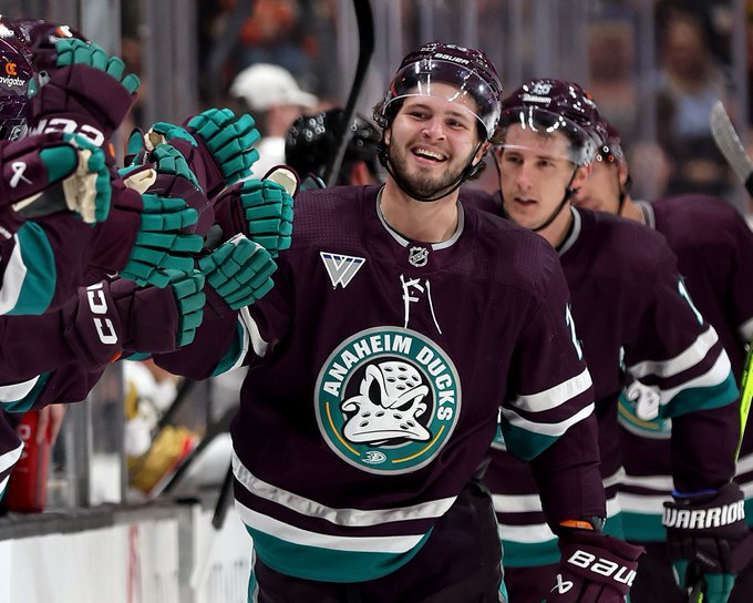 Mason McTavish smiles while high-fiving his teammates at the bench in an Anaheim Ducks alternate uniform. 