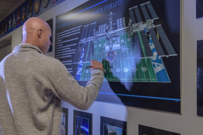Josh Dobbs autographs a poster depicting a graphic that compares the size of the International Space Station to the size of an American football field.