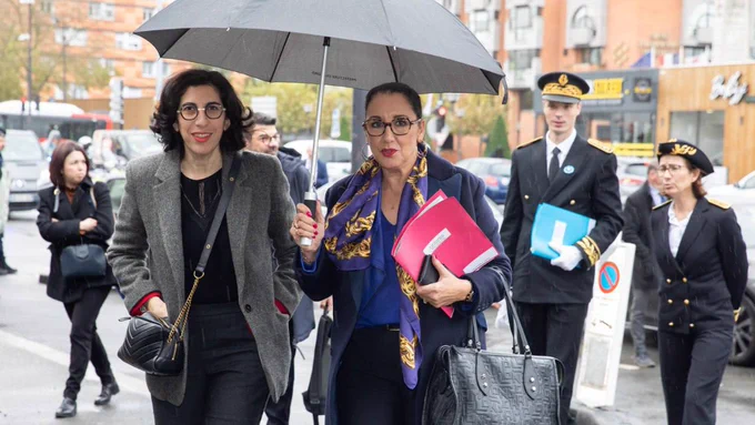 La photographie est prise en extérieur dans une rue de Roubaix.
Fadila Khattabi et Rima Abdul Malak marchent côte à côte. Fadila Khattabi tient un parapluie. Derrière elles marchent plusieurs personnes.