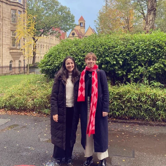 Anna and Hannah are stood in front of university buildings, looking at the camera and smiling