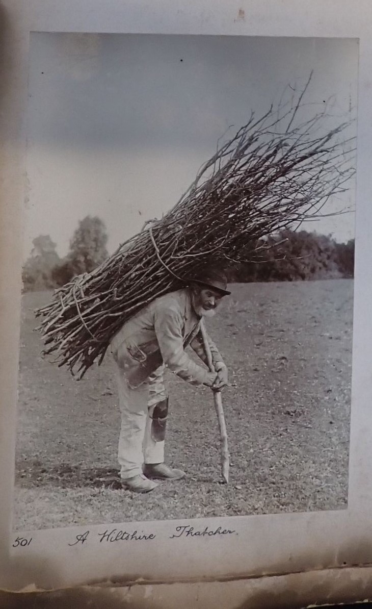Photograph of an old man, bent under a load of sticks he is carrying on his back and leaning on a stick.