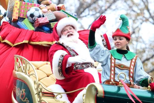 Santa Claus participates in a local Christmas parade along with an elf. 