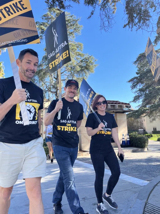 Three people, including SAG-AFTRA TV/Theatrical Negotiating Committee member Charlie Bodin, on the picket line. They carry SAG-AFTRA ON STRIKE signs.