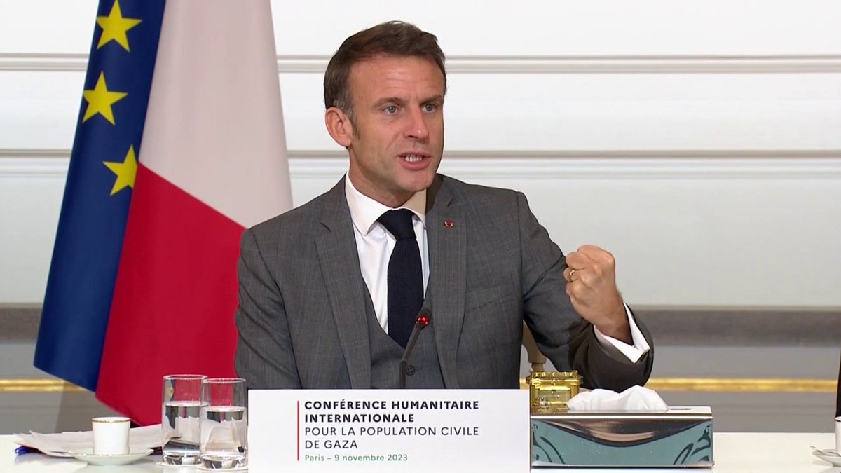 French President Emmanuel Macron speaks at a podium with a sign reading 'CONFÉRENCE HUMANITAIRE INTERNATIONALE POUR LA POPULATION CIVILE DE GAZA - Paris - 9 novembre 2023', with the French and EU flags visible behind him.
