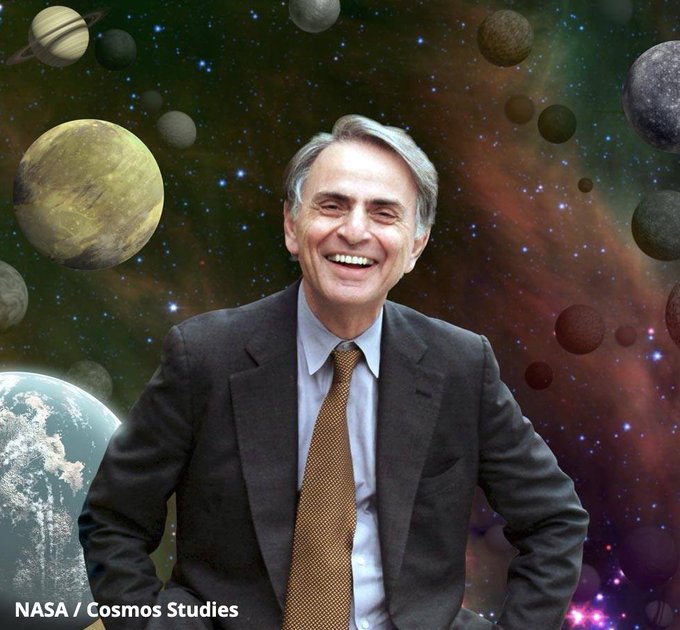 A digital rendering of Carl Sagan smiling at the viewer; he's wearing a suit and is sitting on planet Earth with a colorful cosmos in the background, filled with stars and other planets.