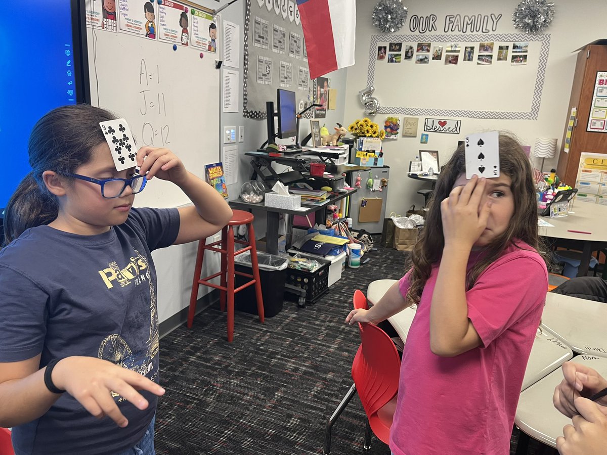Icenhower4VAISD's tweet photo. Practicing our math facts with “what’s the number?” Two friends hold an unknown card on their head and another friend tells them the product. Seeing their friends card and knowing the product, they guess the card on their head!! #wedomath #ThePrestonPride https://t.co/gqElc9d437