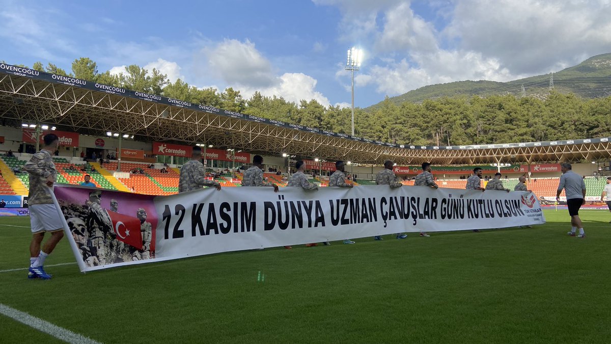 Alanyaspor's tweet photo. Takımımız ısınmaya askeri kamuflaj üniforma ve ‘12 Kasım Dünya Uzman Çavuşlar Günü kutlu olsun’ yazılı pankartla çıktı. https://t.co/7BUcnDehhK