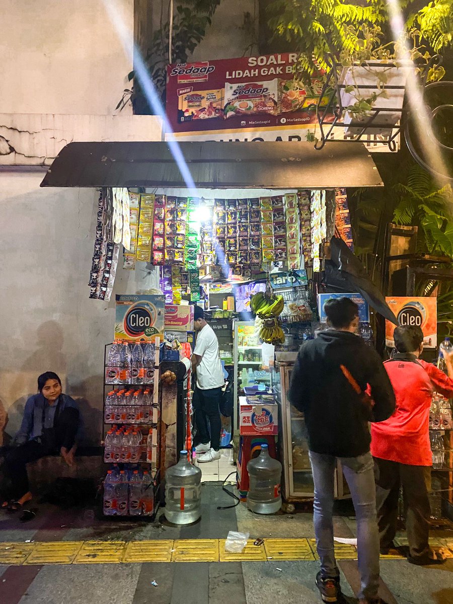 briankhrisna's tweet photo. Biasanya, sepulang kerja, saya punya kebiasaan kecil. Yaitu, mampir di warung-warung kopi pinggir jalan.

Saya tidak tau sejak kapan saya menyukai hal-hal yg menurut saya di beberapa tahun lalu adalah hal yg aneh. Duduk sambil menghisap 234, atau marlboro kretek murah, dan satu gelas kopi jagung seharga 3000 rupiah.

Tapi, justru di tempat inilah saya menemukan banyak hal unik. Sesuatu yg dulu kerap saya lewatkan selepas lelah pulang bekerja.

Di tempat ini, saya bisa melihat gigih kerja keras orang2 yg selama ini selalu terlewatkan di mata saya. Mereka yg sebenarnya bisa tiba2 berubah menjadi seperti seorang karib lama hanya dari berbagi sebatang kretek. 

Mereka yg berbagi masalah hidupnya sendiri, lalu menertawakannya; Seakan bagi mereka hidup ini hanyalah tentang bahagia, sedih, dan di sela-selanya diisi dengan numpang mampir minum kopi.

Di tempat ini, saya jarang sekali melihat keangkuhan, rasa ingin pamer jabatan, atau juga permintaan puji-pujian atas segala pencapaian di sela2 topik pembicaraan.

Di tempat ini, mereka justru membicarakan banyak hal yg jauh lebih menarik. Tentang kabar angin satpol PP yg akan razia di akhir pekan, tentang obrolan politik sekelas RT/RW, tentang sulitnya mengurus berkas di kelurahan, tentang customer ojek online yg kepalang keparat, dan masih banyak lagi.

Garis besarnya, mereka membicarakan tentang hidup mereka yg rasanya luar biasa keras jika dibandingkan dengan hidup saya. Namun mereka tampak sudah begitu terbiasa.

"Soal seragam, mungkin kita beda, Bang. Tapi soal kemampuan mencari nafkah, saya berani di-adu dengan abang."

Kata salah satu bapak tua yg duduk di sebelah karung besarnya yang berisi botol-botol pelastik, kepada saya. 

Saya sangat senang mendengar kisah2 mereka yg tampak asing di hidup saya. Sebab, ketika mendengar cerita2 mereka, saya jadi semakin yakin bahwa sebenarnya kami semua ini sama. Hanya pelumas dari roda-roda bergigi yg bergerak tanpa henti di sebuah kota yg bernama, Jakarta.

Hanya robot yg bekerja tanpa henti demi bisa hidup satu hari lagi-- setiap hari.

Saya mungkin bukan motivator handal. Tapi jika suatu saat hidupmu sedang terasa kepalang keparat, cobalah berhenti sebentar, lalu mampirlah di warung-warung kopi pinggir jalan.

Duduk, lalu coba nikmatilah bagaimana cara kota ini bernapas di sela-sela keriuhannya.