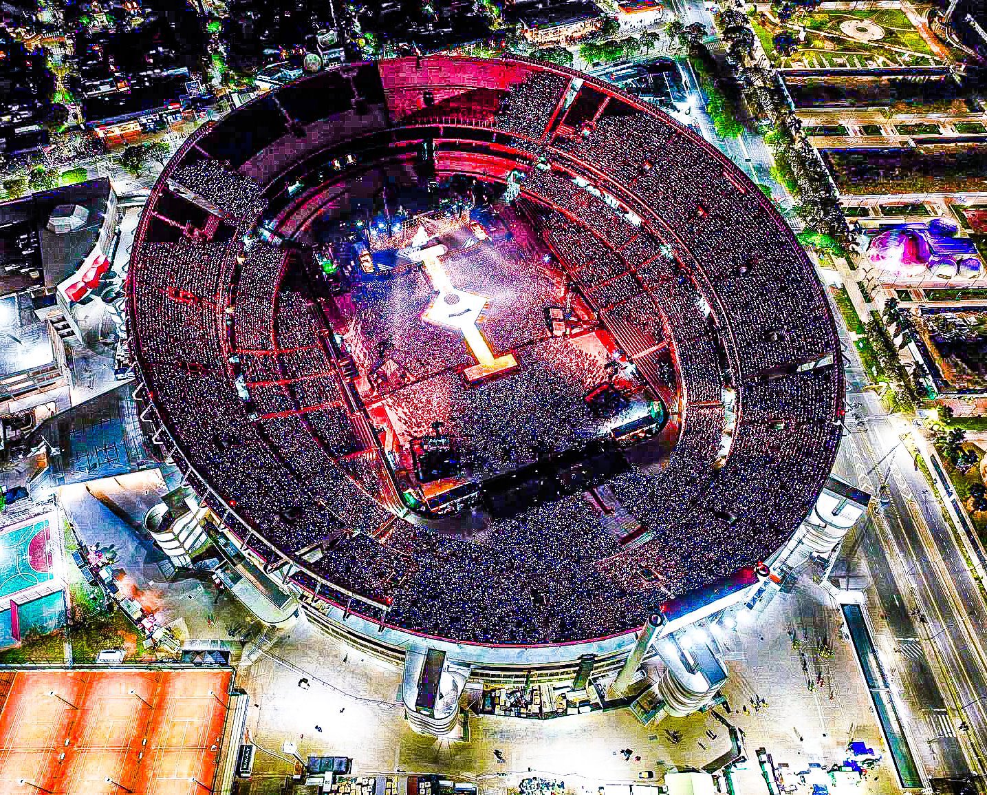 Vista aérea del estadio River Plate lleno de fans durante un concierto, con luces brillantes y un ambiente energético.