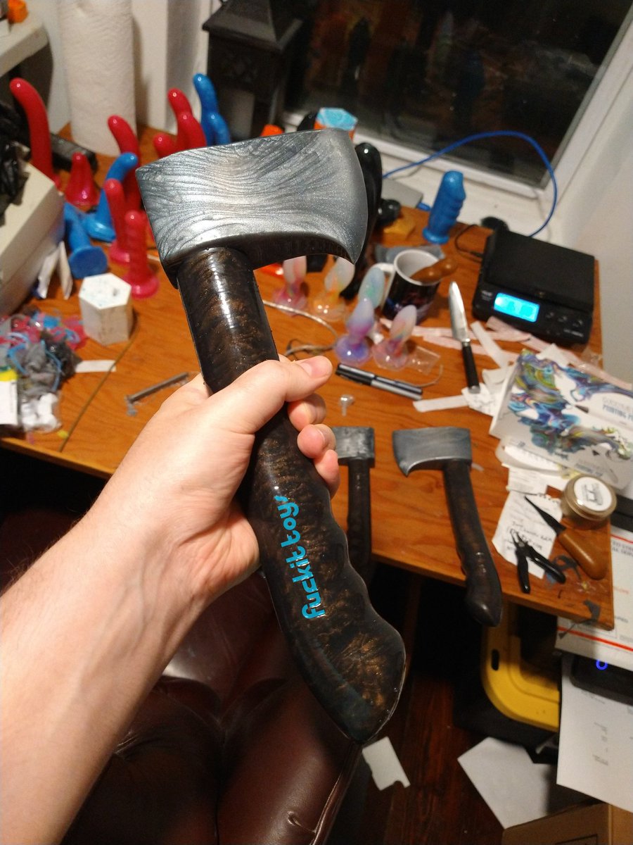 A silicone axe with a hand-grip designed to stimulate the g-spot or prostate, with raised bumps between where the fingers would hold it. The handle is a deep walnut brown shimmer, and the head is a shimmery silver.