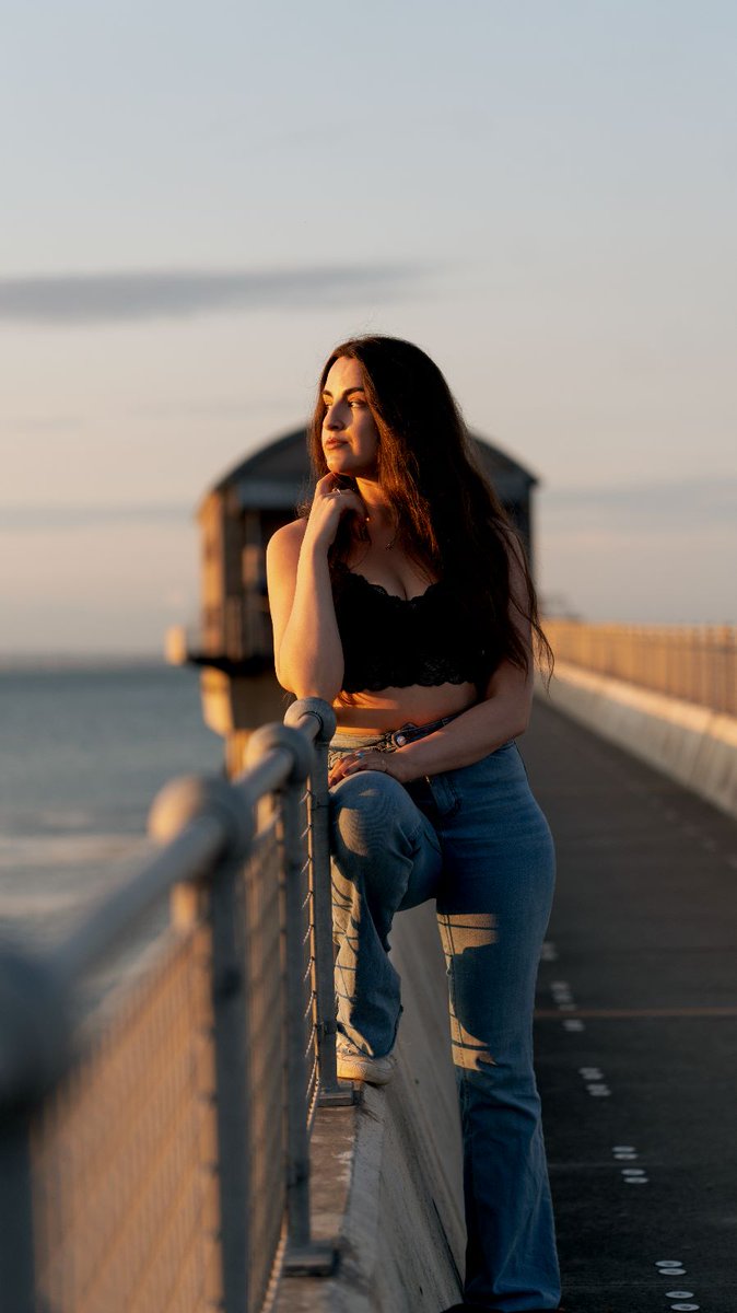 CzoborN's tweet photo. "Bathed in the gold of the setting sun, her gaze weaves tales of longing and adventure. Against the faded pier, she is a beacon of dreams, lost yet anchored. Her story is a symphony of light and shadow, a melody that lingers long after the sun's farewell." https://t.co/WGSIZv5sQd