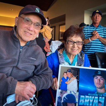 Bryan Woo's sit in a suite at Oracle Park and hold a sign with photos of Bryan as a child and with his 