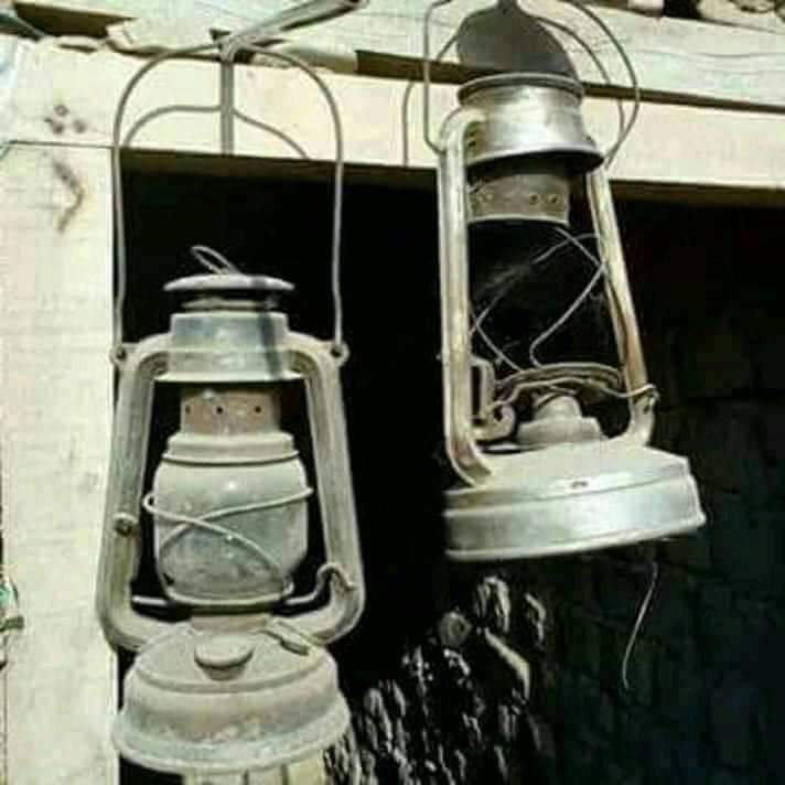 UrduVirsa's tweet photo. سردیوں میں آندھی یا بارش کے ساتھ ہی سب سے پہلی آواز یہ آتی کہ لالٹین کا تیل دیکھو، اگر نہیں تو بھاگ کر نکڑ والی دکان سے آٹھ آنے کا تیل ڈلوا لاؤ۔ بانس کی پرانی چھڑی کے ساتھ چلنے والے بابے موچی نے گھی والے کنستر میں مٹی کا تیل رکھا ہوتا تھا سردیوں  میں لالٹین میں تیل ڈلواتا اور دوبارہ گھر کی طرف دوڑ لگا دیتا۔ ہم دو بھائی اور ایک بہن ایک کمرے میں سوتے تھےاکثر اس بات پر جھگڑا ہوتا کہ لالٹین کس کے قریب رکھی جائے گی کیونکہ سبھی اسکول جاتے تھے اور کسی نہ کسی کو اپنا ہوم ورک کرنا ہوتا تھا۔
ہماری لالٹین اسی چھوٹی شیلف پر رکھی جاتی تاکہ روشنی سارے کمرے میں جائے۔ میں کبھی کبھار لالٹین کا فیتہ زیادہ اوپر کر دیتا تو فوراً امی جی کی آواز آتی:’’نیچے کرو، ورنہ لالٹین کا شیشہ دھوئیں سے کالا ہو جائے گا۔‘‘
کبھی کبھار رات گئے لالٹین کا فیتہ ختم ہو جاتا تو ہم فوراً کسی پیالی یا چراغ میں سرسوں کا تیل ڈالتے، خود ہی روئی کا ایک فیتہ بناتے اور لالٹین کا متبادل تیار کر لیتے لیکن اس میں مسئلہ یہ تھا کہ سیاہ دھوئیں کے نشانات دیوار پر لگ جاتے اور یہ نشان تب تک رہتے جب تک دوبارہ چونے سے تیار ہونے والا رنگ (کلی) نہ اُس پر پھیر دیا جاتا۔ عید وغیرہ پر چونے میں نیل ڈال کر دیواروں پر رنگ کیا جاتا۔ اسی طرح پیتل کے برتنوں کو بھی خاص تہواروں کی مناسبت سے نئے سرے سے پالش کیا جاتا تھا۔
میں اکثر اپنی تختی سونے سے پہلے لکھتا تھا۔ آپی ہمیشہ اس وجہ سے ڈانٹتی کہ یہ بدتمیز اپنا اسکول کا کام صبح کے وقت کیوں نہیں کرتا۔
میں آپی کے ہر روز کے احتجاج کے باوجود لالٹین نیچے زمین پر رکھتا، تھیلے نما بستے میں سے قلم اور دوات نکالتا اور لکڑی سے بنی تختی پر سبق لکھنا شروع کر دیتا۔ اس وقت یہی کُل متاع ہوتی تھی: قلم، سیاہی، دوات، سلیٹ اور سکہ وغیرہ۔ مَیں تختی پر لائنیں لگانے کے لیے سکہ ہمیشہ کسی ریڈیو کی بیٹری توڑ کر ہی نکالا کرتا تھا۔
اس وقت موم بتیاں بھی تھیں لیکن مٹی کا تیل سستا ہونے کی وجہ سے ہم لالٹین اور دیا ہی استعمال کرتے رہتے۔ کبھی کبھار ہم موم بتی بھی لے آتے۔ 
جس دن بھی بارش تیز یا مسلسل ہوتی تو چھت سے پانی ٹپکنا شروع ہو جاتا۔ جہاں جہاں سے پانی ٹپکنا شروع ہوتا، ہم بہن بھائی اس کے نیچے برتن، بالٹی یا پرات وغیرہ رکھتے جاتے تاکہ پانی اس میں جمع ہو۔ میں رضائی سے منہ نکال کر یہ اندازہ لگاتا رہتا کہ چھت سے ٹپکنے والا اگلا قطرہ کس برتن میں گرے گا۔ لالٹین کی مدھم روشنی، تیز ہوا کی سرسراہٹ، لحاف کے اندر خود کو گرم رکھنے کی کوشش، بارش کی رم جھم، کچی چھت پر گرتی اور رقص کرتی بارش کی بوندوں کی آواز، بادلوں کی گھن گرج اور چھت سے ٹپکتے قطرے ایک جادوئی ماحول پیدا کر دیتے تھے۔ لیکن تب مجھے یہ معلوم نہیں تھا کہ میں آٹو ہیٹڈ کمروں، نرم گداز صوفوں،  قالینوں اور جرمن میڈ رضائیوں کے ہوتے ہوئے بھی ان کی چاہت کروں گا، وہ کاغذ کی یاد کروں گا وہ بارش کا پانی یاد کروں گا۔
 میں بہن بھائیوں میں سب سے بڑا تھا اور ڈر بھی مجھے ہی سب سے زیادہ لگتا تھا۔ بھائی بہن بھی میری اس عادت سے تنگ تھے۔ کمرے کے باہر کھلا صحن تھا اور اس کے بعد ٹوائلٹس آتے تھے۔ سردیوں میں مَیں اکیلا وہاں تک جانے سے ڈرتا تھا اور جب تک کوئی لالٹین پکڑ کر دروازے تک ساتھ نہیں جاتا تھا، میں ضد لگا کر بیٹھا رہتا تھا۔
ہمارے گھر روئی ہمیشہ اس وجہ سے بھی رہتی کہ نانا جی نے آٹا پیسنے کی مشین کے ساتھ ساتھ روئی دھننے کی مشین ( پینجہ) بھی لگا رکھی تھی۔ ان کے گھر رضائیاں بھروانے والوں کا ہمیشہ تانتا بندھا رہتا تھا اور امی بھی دن کے وقت ادھر ہی رہتیں اور کرائے کے طور پر لی جانے والی روئی میں سے کچھ گھر لے آتیں۔
ہم چھوٹے چھوٹے تھے تو نانا جی کے گھر امی جی سوت خود کاتتی تھیں۔ میں بھی ایک باریک چھڑی (کانے) کی مدد سے روئی کی پونیاں بنا کر انہیں دیتا رہتا اور وہ اُسے چرخے کے کتلے پر چڑھا کر اس سے دھاگا بناتیں۔ مجھے سب سے زیادہ مزہ چرخہ چلانے میں آتا کیوں کہ وہ ٹائر کی طرح گھومتا جاتا اور ایک سیٹی کی سی مخصوص آواز پیدا ہوتی جاتی۔
جرمنی کی یخ بستہ راتوں میں جب بھی کبھی رات کو موسلا دھار بارش ہوتی ہے یا تیز ہوا مخصوص آوازیں پیدا کرتی ہے تو مجھے بے ساختہ اپنا ماضی، ٹپکتی ہوئی چھت، لالٹین، دیا، تختی، امی جی کا چرخہ اور کوہ قاف کی کہانیاں یاد آنا شروع ہو جاتی ہیں۔
مجھے پہلی جماعت کا وہ قاعدہ یاد آ جاتا ہے، جس کی سب سے مشہور نظم بلبل کا بچہ تھی۔ اب مجھے لگتا ہے کہ وہ بلبل کا بچہ میں تھا، جو کھاتا تھا کھچڑی، پیتا تھا پانی، اک دن اڑایا، واپس نہ آیا۔۔۔

امتیاز احمد
منقول
