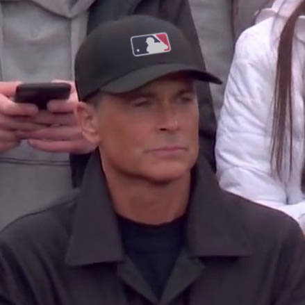 Rob Lowe, looking serious, wearing an MLB hat.