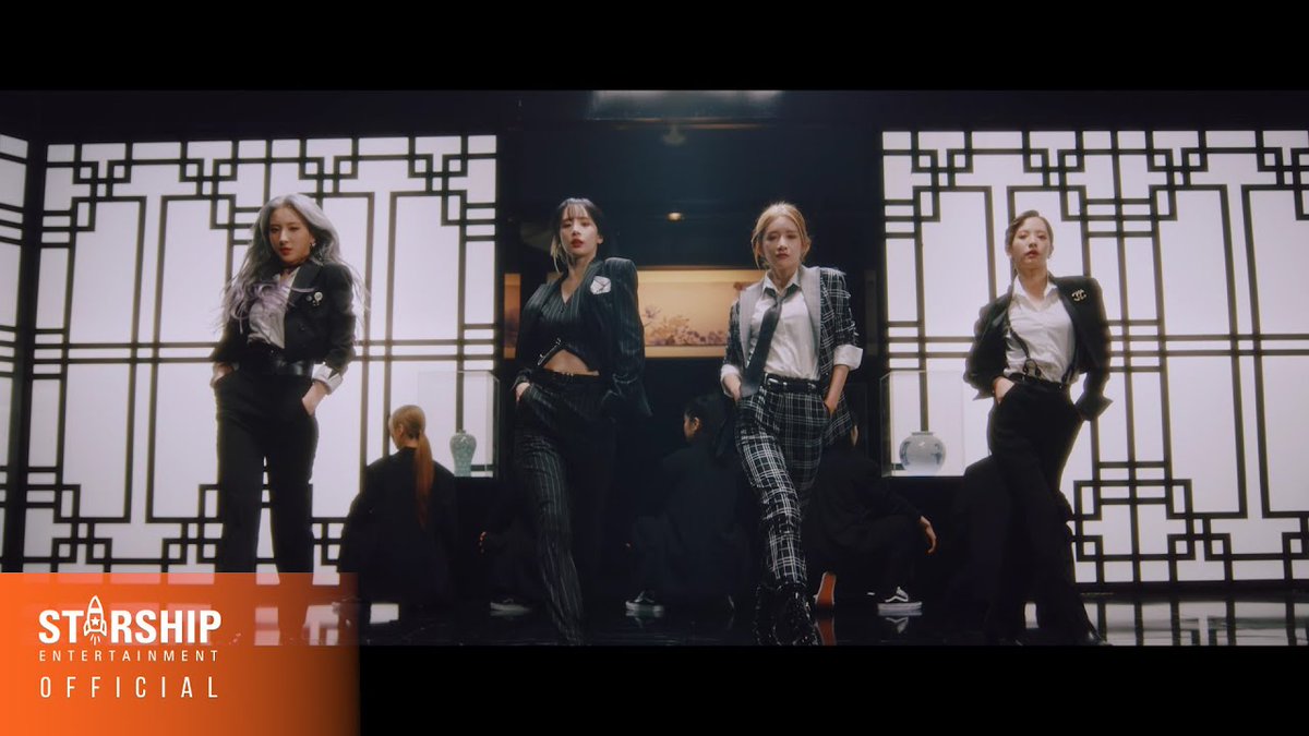Four women in stylish black, white, and plaid suits pose confidently in a room with Asian-inspired lattice screens, with a 'STARSHIP ENTERTAINMENT OFFICIAL' logo in the corner.