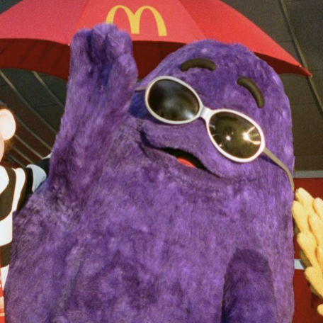a picture of me (Grimace) being happy and waving goodbye with my right hand. I am wearing very cool shades. There's a red umbrella behind me with a McDonald's logo. Hamburglar and Birdie are standing next to me but we can barely see them as I do not know out to crop a picture properly.