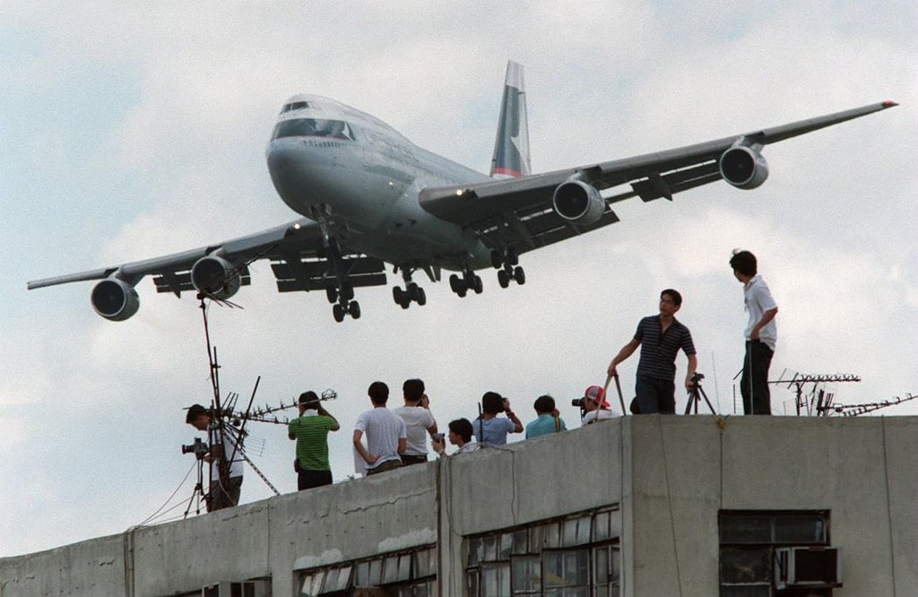 GinieSigonney's tweet photo. Kaï Tak fut fermé le 6 juillet 1998 .

Il n'y avait qu'une seule piste à Kai Tak, orientée à 135 et 315 degrés, en fonction de l'approche, appelée 13/31. Piste 13 (direction sud-est) et Piste 31 (direction nord-ouest). « La 13 » était utilisée la plupart du temps, car le vent de sud-est est dominant à Hong-Kong.

L'approche d'atterrissage employant « la 13 » à Kai Tak était spectaculaire et connue du monde entier. Pour y atterrir, l'avion devait prendre une trajectoire initiale nord-est pour la descente.
L'avion survolait le port à très basse altitude, et ensuite, des secteurs occidentaux de Kowloon, très dense en population. Un système d'aide à navigation « IGS » (un ILS modifié) fut installé en 1974 pour faciliter cette partie de la descente sur la 13.
Lorsque l'avion atteignait la colline sur laquelle était placé un damier rouge et blanc, servant de balise d'orientation lors de l'approche finale, les pilotes devaient effectuer un virage à vue de 47° pour l'alignement final avec la piste. L'avion n'est alors qu'à deux milles marins de l'atterrissage, à une altitude de moins de 330 m lors de ce virage: généralement, l'avion entamait le virage final à une altitude d'environ 200 m et en sortait à une hauteur d'environ 40 m. L'approche était déjà délicate pour l'atterrissage sur la 13 avec les vents latéraux normaux, car même si la direction du vent reste constante, elle change relativement à l'avion lors du virage de 47°. L'atterrissage devenait un défi plus grand encore quand les vents latéraux du nord-est étaient forts et de
haute variabilité, notamment pendant les typhons, fréquents dans cette région. La chaîne de montagnes au nord-est de l'aéroport fait également changer considérablement la vitesse et la direction du vent, changeant par là-même la dérive de l'avion.
L'observation d'un Boeing 747 volant à pleine charge, effectuant un tel virage à basse altitude, tout en prenant un grand angle de crabe pour compenser la dérive pendant son approche finale, pouvait être impressionnante. En dépit de la difficulté, la 13 était néanmoins préférée la plupart du temps à cause de la direction du vent dominant à Hong-Kong.
En raison du virage dans l'approche finale, aucun atterrissage sur la piste 13 ne pouvait utiliser le système d'atterrissage aidé par instruments
« ILS », les pilotes devant impérativement suivre une approche visuelle. 
.
.
.
#aviation #avgeek #aviationlovers #aviationphotography #Pilot #pilotlife #aviation4u #aviatiingeek 

©️Wikipedia 
🎬Credit to author