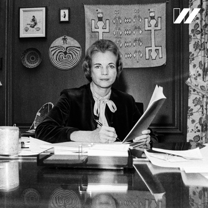 A black and white image of Sandra Day O’Connor sitting at a desk, looking into the camera. There is a white “w” U S O W logo in the top right corner.