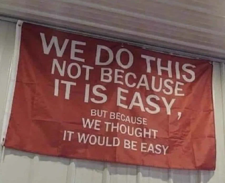 writing on a flag: 
"WE DO THIS NOT BECAUSE IT IS EASY, but because we thought it would be easy"