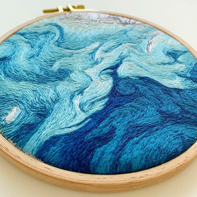 This embroidered image was inspired by imagery gathered by NASA’s Earth-observing satellites, many of which study ocean color. Embroidery artist Danielle Currie of Satellite Stitches finds inspiration in our agency’s look at the ocean. Credit: Danielle Currie of Satellite Stitches. This embroidered image is surrounded by a brown, wooden frame. To the left, the image shows light blue threads in the shape of waves. They continue across the circular piece with white thread in the top showing snow covered land. In the bottown, dark blue threads move in waves, showing movement of water. 