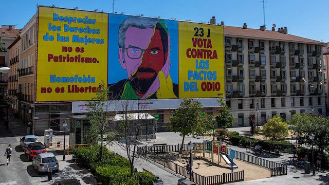 CarlaAntonelli's tweet photo. Una lona gigante en la Plaza Pedro Zerolo de Chueca, llama a votar contra “los pactos del odio” de PP y Vox, una mano arranca una máscara que tiene el rostro de Feijóo y que debajo esconde la cara de Santiago Abascal, que lleva una cerilla encendida en la boca #23J #VotaConOrgullo https://t.co/D3omem5Dv8 vía @el_pais