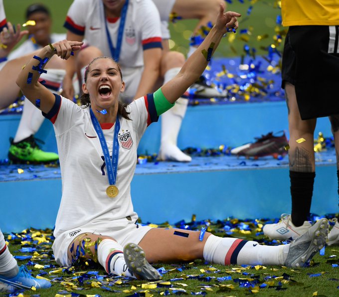 De él una Jugadora Estadonidens Vestida de Blanco.  Se trata de que los últimos momentos se organicen como una celebración.  a su quelo cuelga es una medalla dorada 