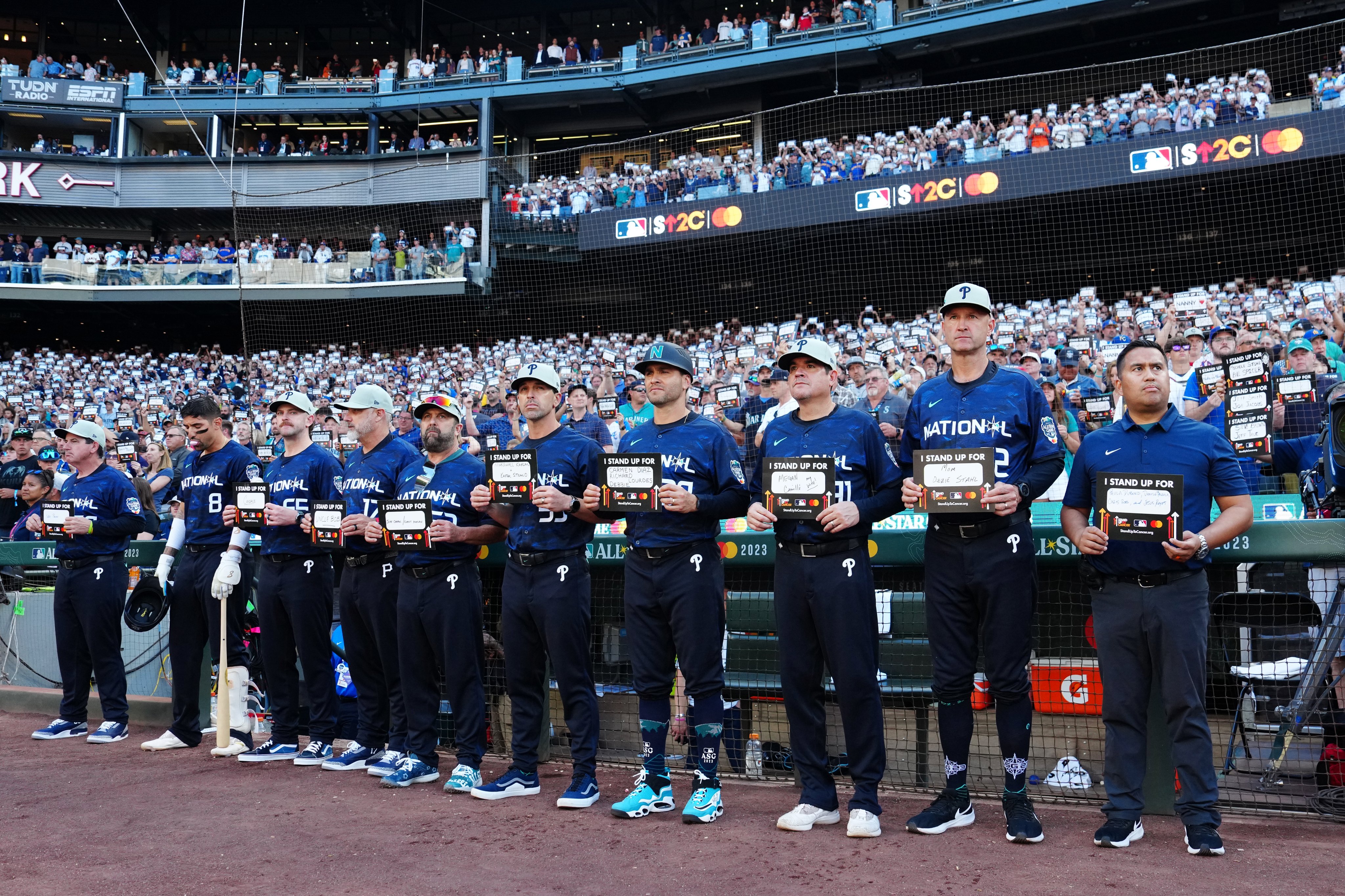 Members of the NL All-Star team hold up Stand Up To Cancer signs prior to the start of the 6th inning at the 2023 All-Star Game.