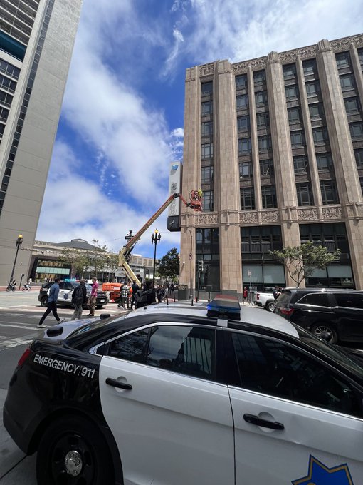SFPD in front of a crane that's taking down the twitter name and logo