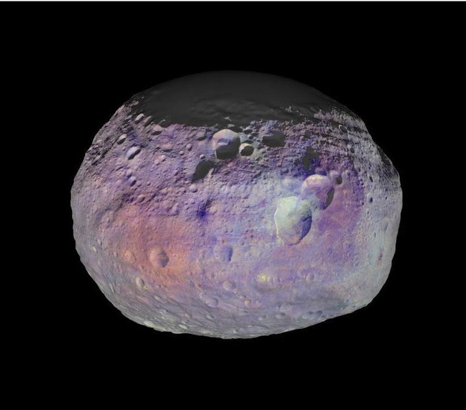 This image of asteroid Vesta taken by the NASA Dawn spacecraft shows the diversity of minerals through color representation. The gray asteroid is seen against black, with splotches of color showing concentrations of different minerals. Craters are scattered across the asteroid.