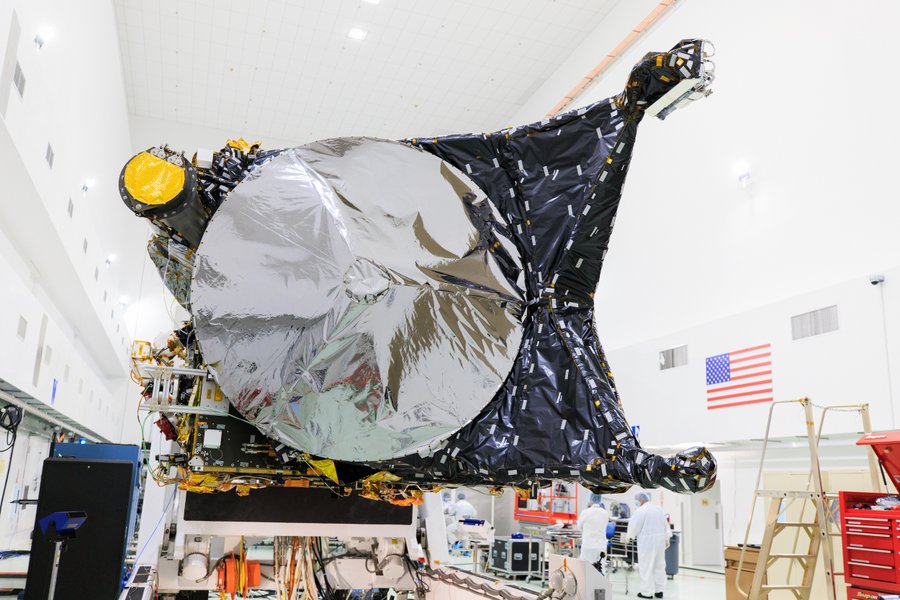 This image was captured at the Astrotech Space Operations facility near the agency’s Kennedy Space Center in Florida. The high gain antenna of NASA’s Psyche spacecraft, which will be used to send and receive signals from home, takes center stage in this photo. The high-gain antenna looks like a large silver saucer-shaped object. A black space blanket is tightly fitted on the spacecraft surrounding the antenna. A few wires are visible near the bottom but much of the spacecraft is covered in blankets. In the faded distance, four team members are busy working in the clean room and various tools and ladders surround them. Credit: NASA/Frank Michaux