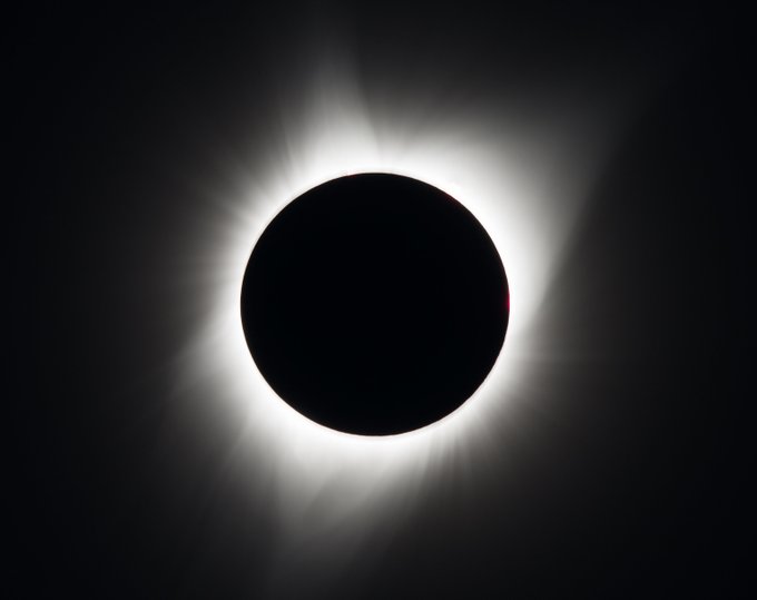 This total solar eclipse, which occurred on Monday, Aug. 21, 2017, was photographed from Madras, Oregon. It appears as a black disk in the sky, encircled by a white ring of light that varies in thickness and intensity around its dynamic and flame-like, shadowy edges. The sky in the background is also black. Source: NASA/Aubrey Gemignani.