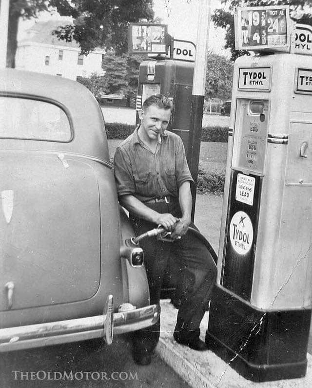Man putting gas in his car while smoking a cigar, 1900s.