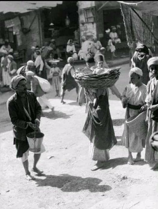 صورة للحياة البغدادية تعود لسنة 1932 لاحد اسواق بغداد يظهر رجل يرش الماء بالجردل امام محله... و هذه طبيعة عامة لاصحاب المحلات آنذاك لتلطيف الجو وللنظافة . كما يظهر طفل يحمل على راسه سلة فيها خبز للبيع ...لا تجد بين الناس من هو حاسر الراس..